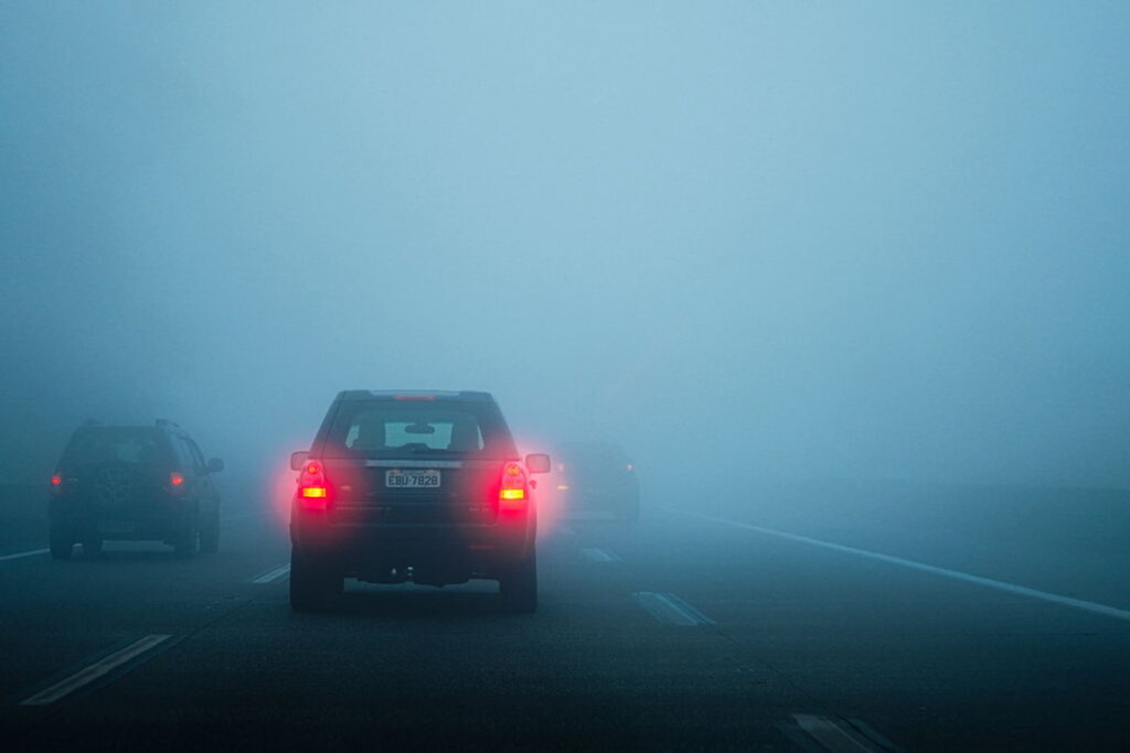 Cars driving through dense fog with limited visibility on a multi-lane road.