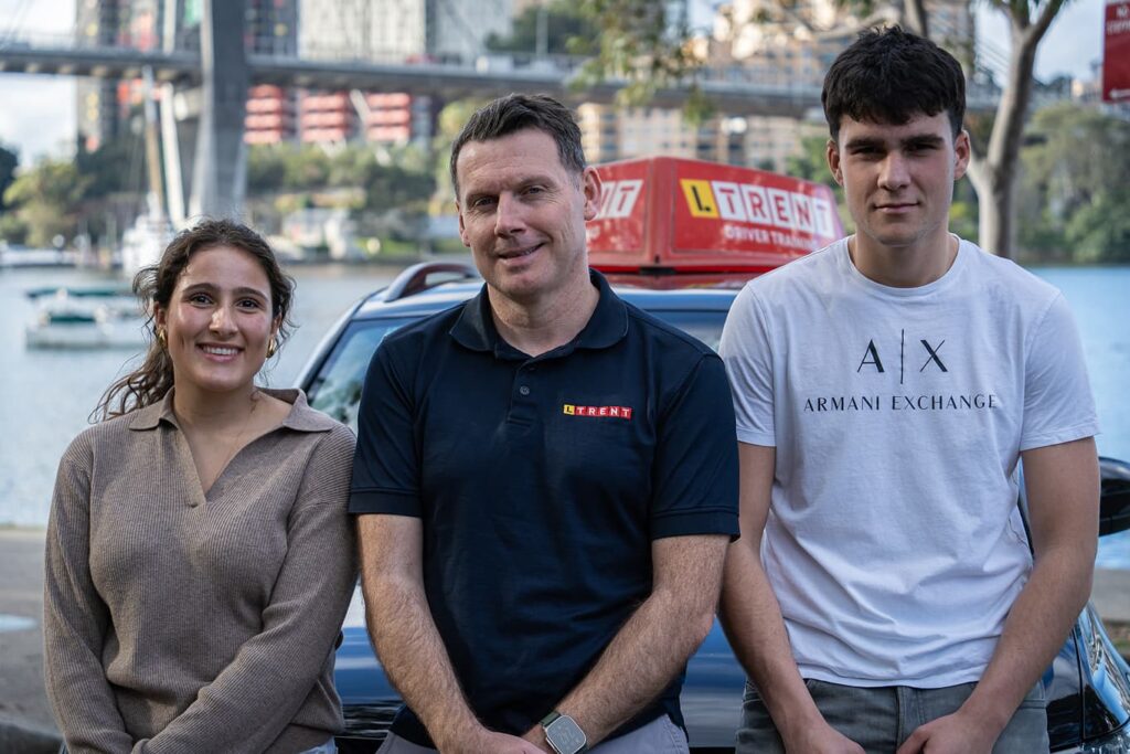 LTrent driving instructor with two students beside a driving school vehicle